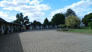 A spacious courtyard with a paved floor, surrounded by buildings with multiple windows and doors, some with outdoor seating. - Orana Windmill Motel (Gilgandra)