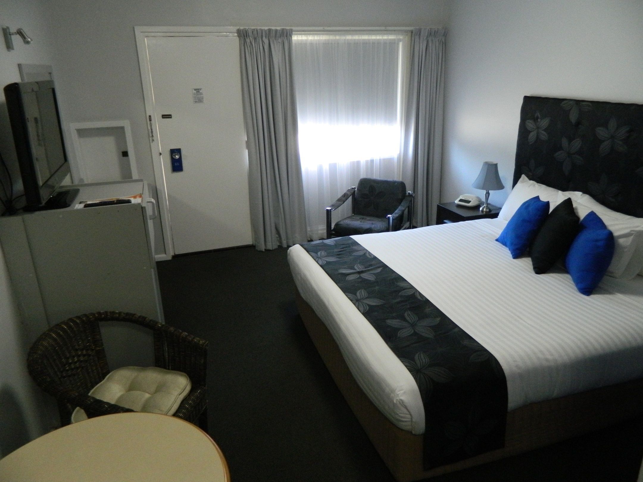 A hotel room with a bed, a chair, a desk, a lamp, and a television.