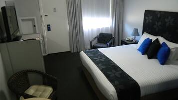A hotel room with a bed, a chair, a desk, a lamp, and a television.