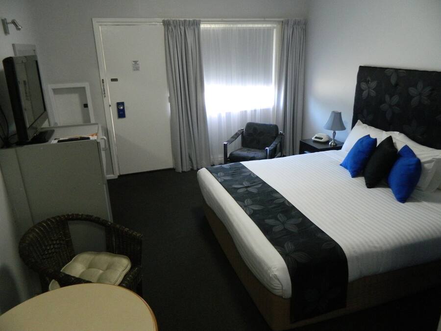 A hotel room with a bed, a chair, a desk, a lamp, and a television.