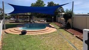 A backyard with a swimming pool, a shaded area, and a fenced yard. - Orana Windmill Motel (Gilgandra)