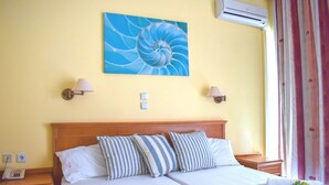 Una cama doble con almohadillas a rayas, un cabecero de madera, dos lámparas de noche, un aire acondicionado de pared y un cuadro de una espiral azul.