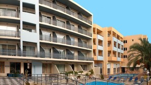 Un hotel de varios pisos con piscina en la azotea, zona de estar al aire libre y una palmera.