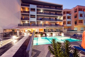 A multi-story hotel with a swimming pool, outdoor seating, and a well-lit entrance. - Kleoniki Mare Hotel (Rethymno)