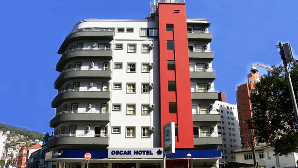 Un hotel de varios pisos con una sección vertical roja destacada, múltiples balcones y una entrada visible con un cartel que dice "OSCAR HOTEL".