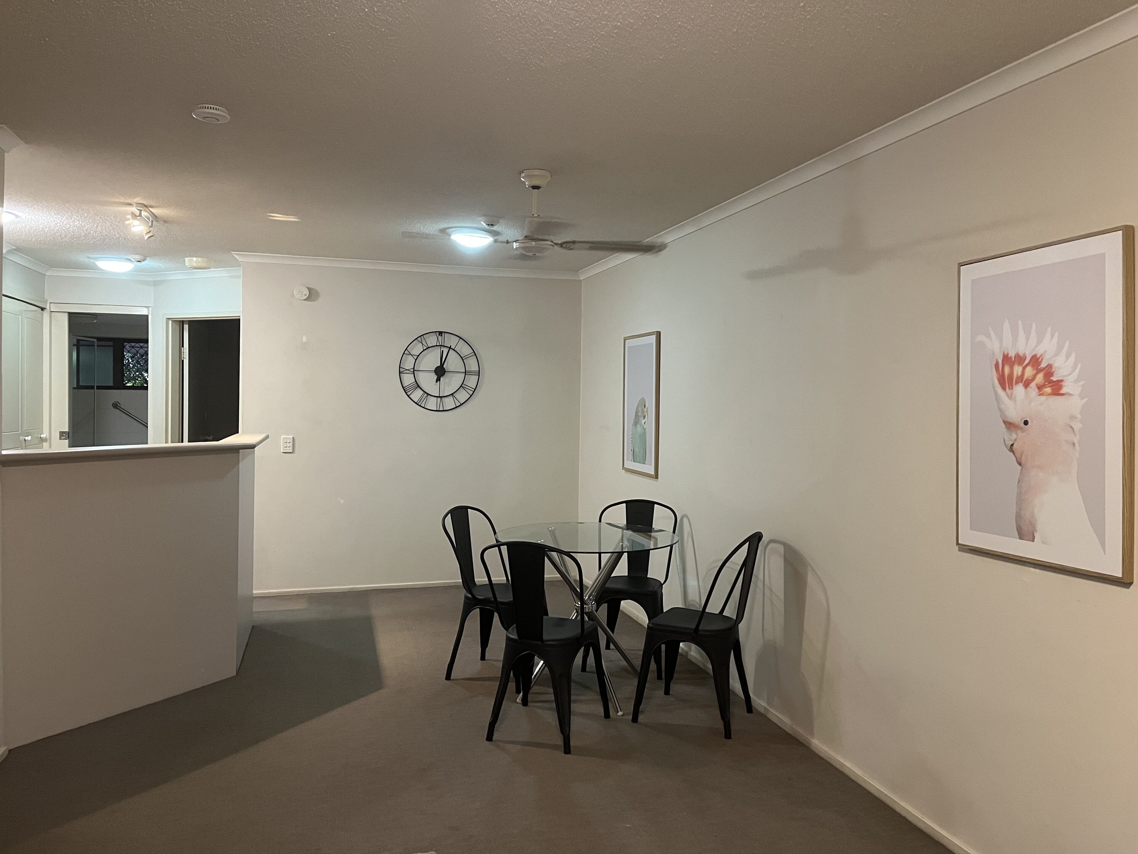 A dining area with a round table and four chairs, a wall clock, and a framed picture on the wall.