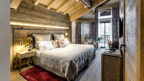 Un dormitorio con una cama grande, vigas de techo de madera, una mesita de noche con lámpara y vistas al exterior a través de una ventana.