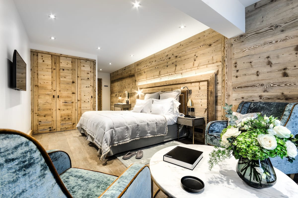 Un dormitorio moderno con una cama grande, paneles de madera, un televisor y una mesa con un libro y flores.