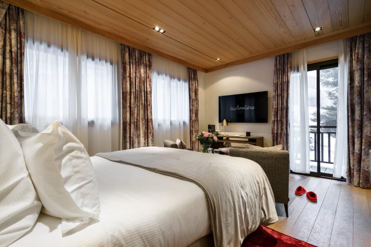 A bedroom with a large bed, a desk, a TV, and a balcony.