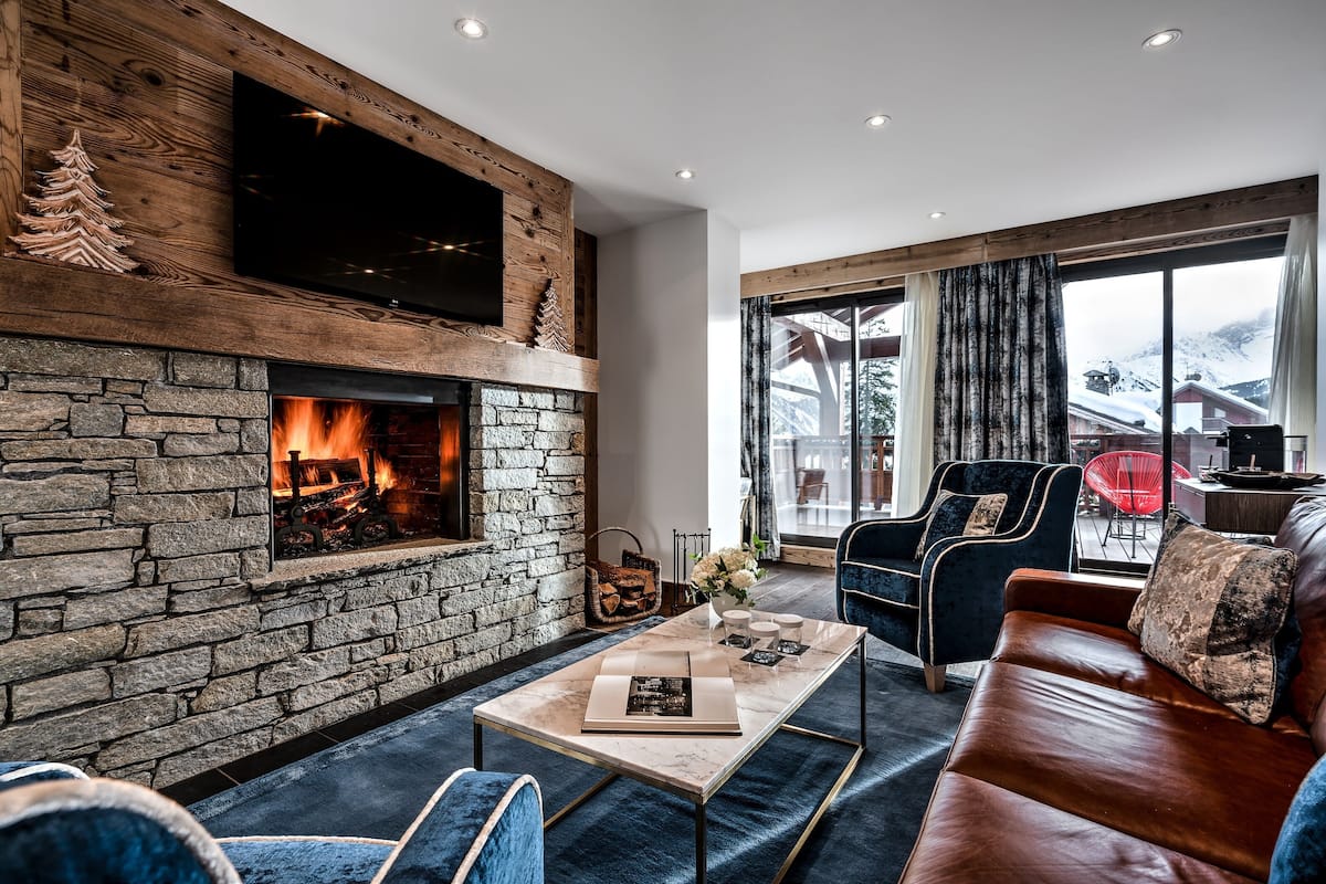 Un salón acogedor con chimenea de piedra, asientos cómodos y un amplio ventanal con vistas al exterior.