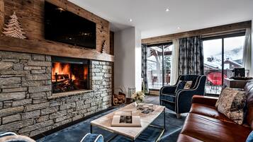 Un salón acogedor con chimenea de piedra, asientos cómodos y un amplio ventanal con vistas al exterior.