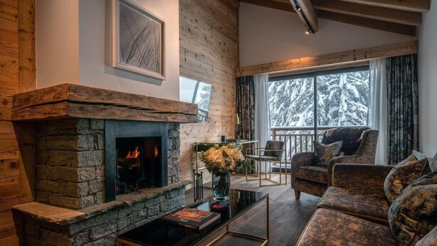 Una sala de estar acogedora con chimenea de piedra, asientos cómodos y vistas a árboles nevados a través de amplios ventanales.