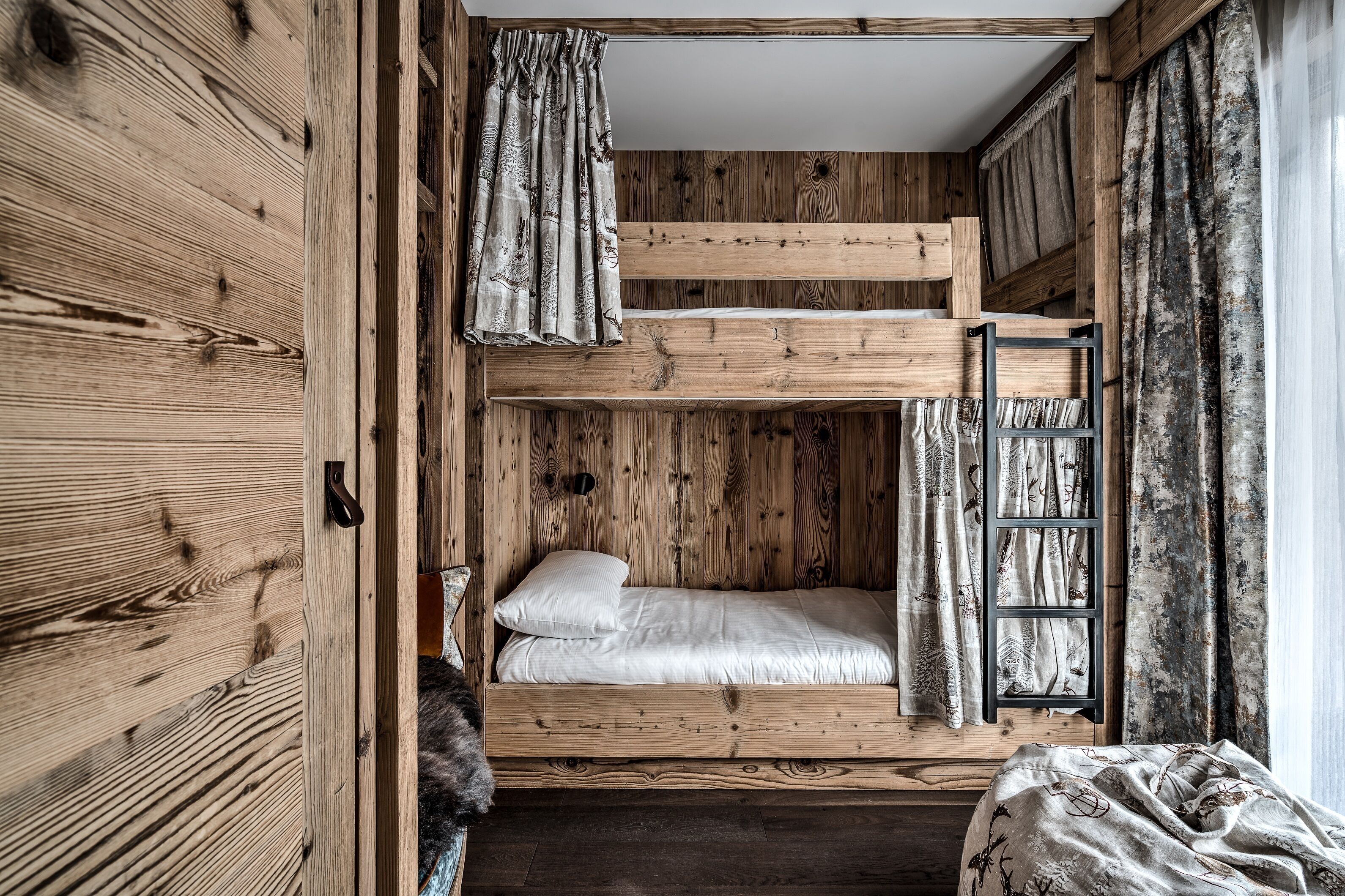 Un lit superposé avec une échelle, des murs en bois et une fenêtre avec des rideaux.