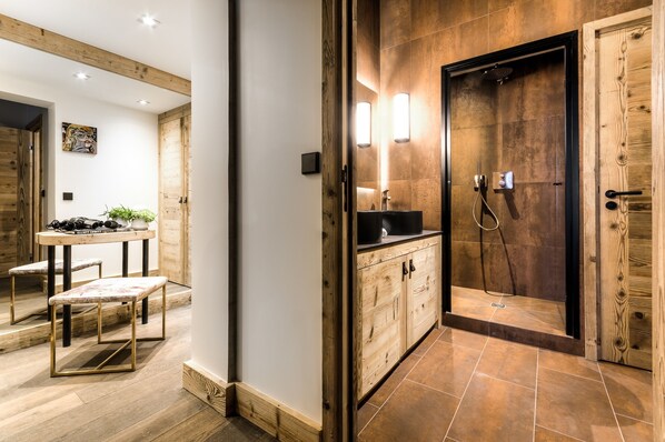 A modern bathroom with a wooden vanity, a shower with a glass door, and a small table with stools.