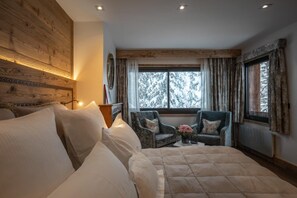 A cozy bedroom with a large bed, a chair, and a window with a snowy view.