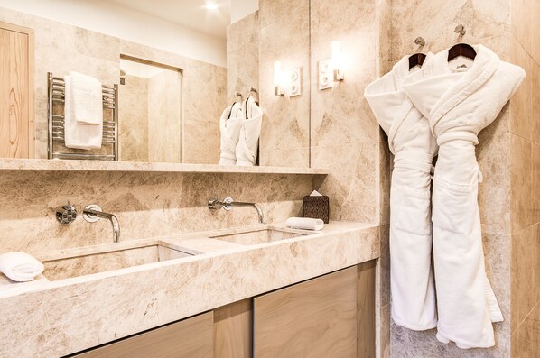 A modern bathroom with two sinks, a mirror, and two white robes hanging on hooks.