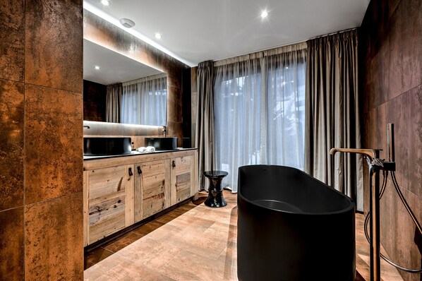 A modern bathroom with a freestanding bathtub, wooden cabinetry, and a large mirror.