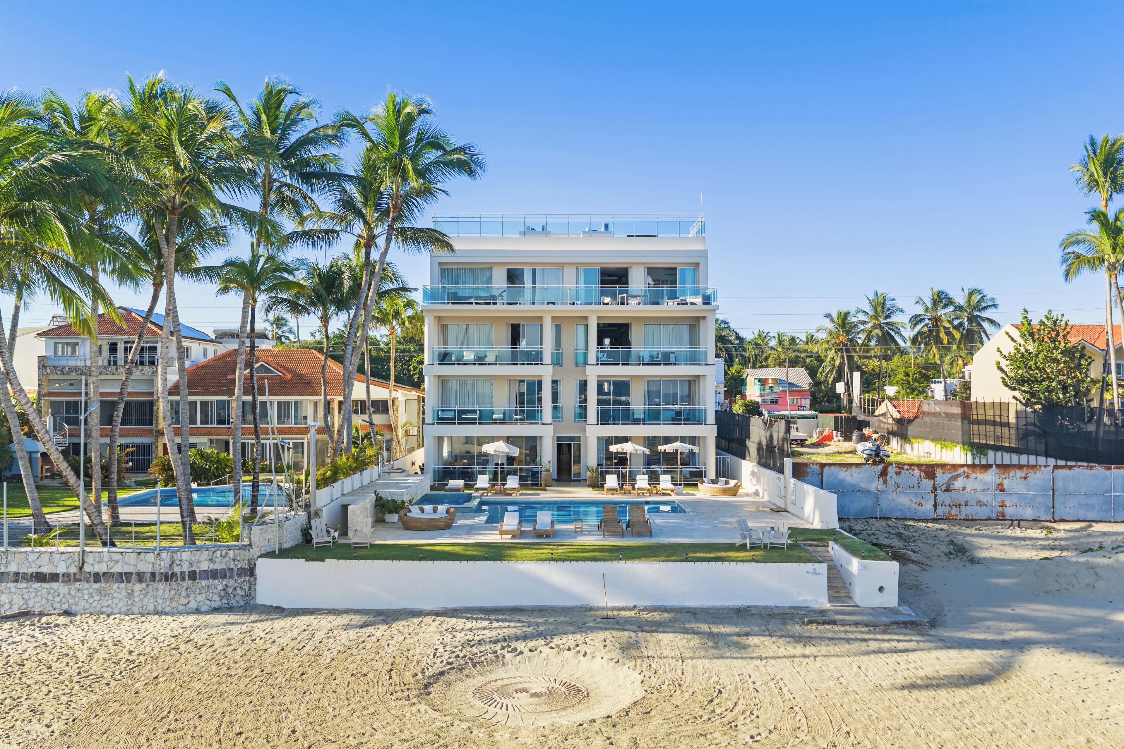 Un hôtel à plusieurs étages doté d’une piscine, de palmiers et d’une plage de sable.