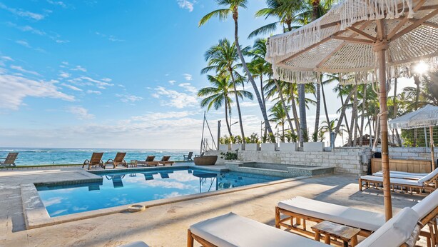 A poolside area with lounge chairs, a wooden deck, and a view of the ocean. - Watermark Luxury Oceanfront All Suite Hotel (Cabarete)