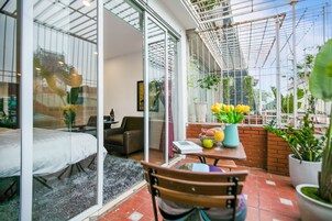 A modern living room with a glass wall, a wooden table with a vase of flowers, and a comfortable seating area.