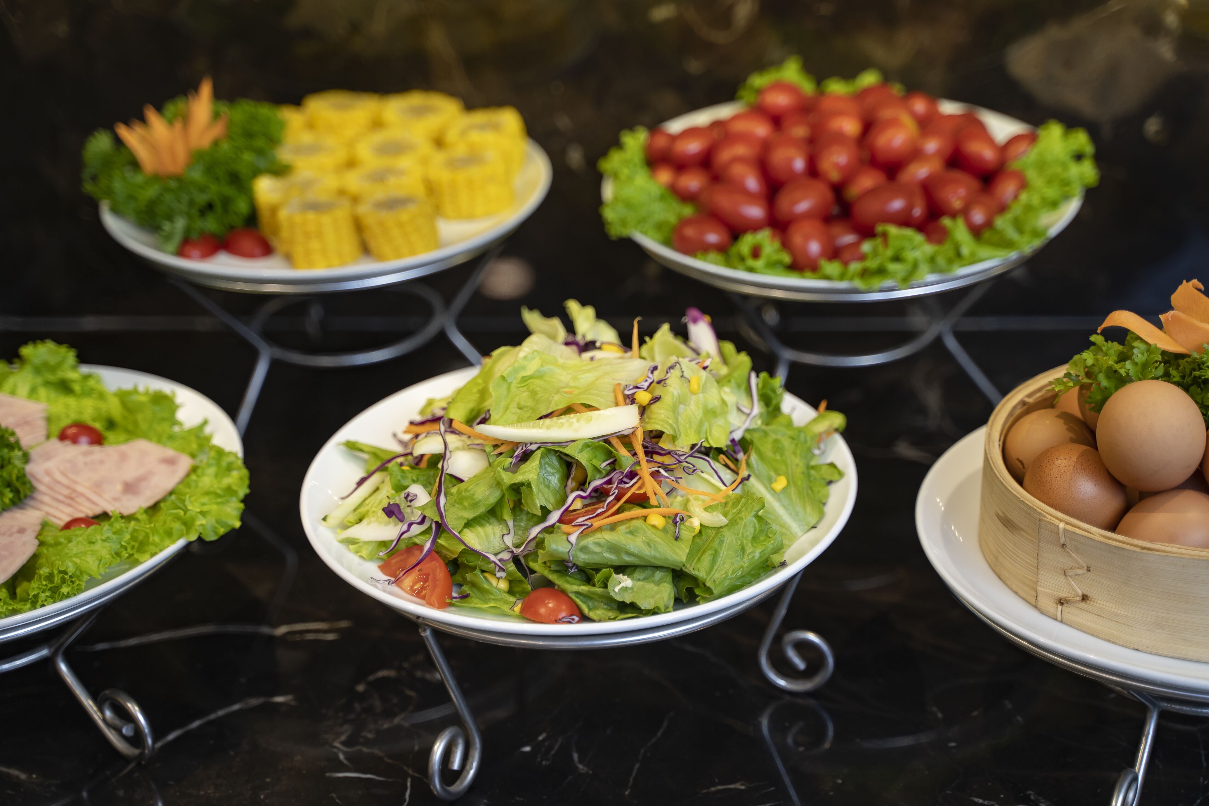 Une table de buffet proposant divers plats, notamment des salades, du maïs, des tomates et des œufs.