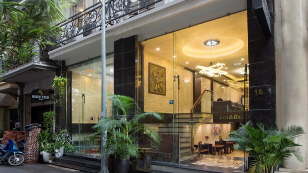 A hotel entrance with a glass facade, outdoor seating, and potted plants. - Splendid Star Grand Hotel & Spa (Hanoi)