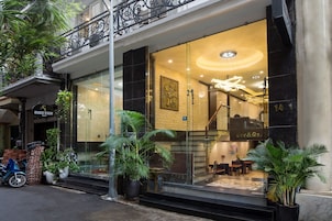 A hotel entrance with a glass facade, outdoor seating, and potted plants.