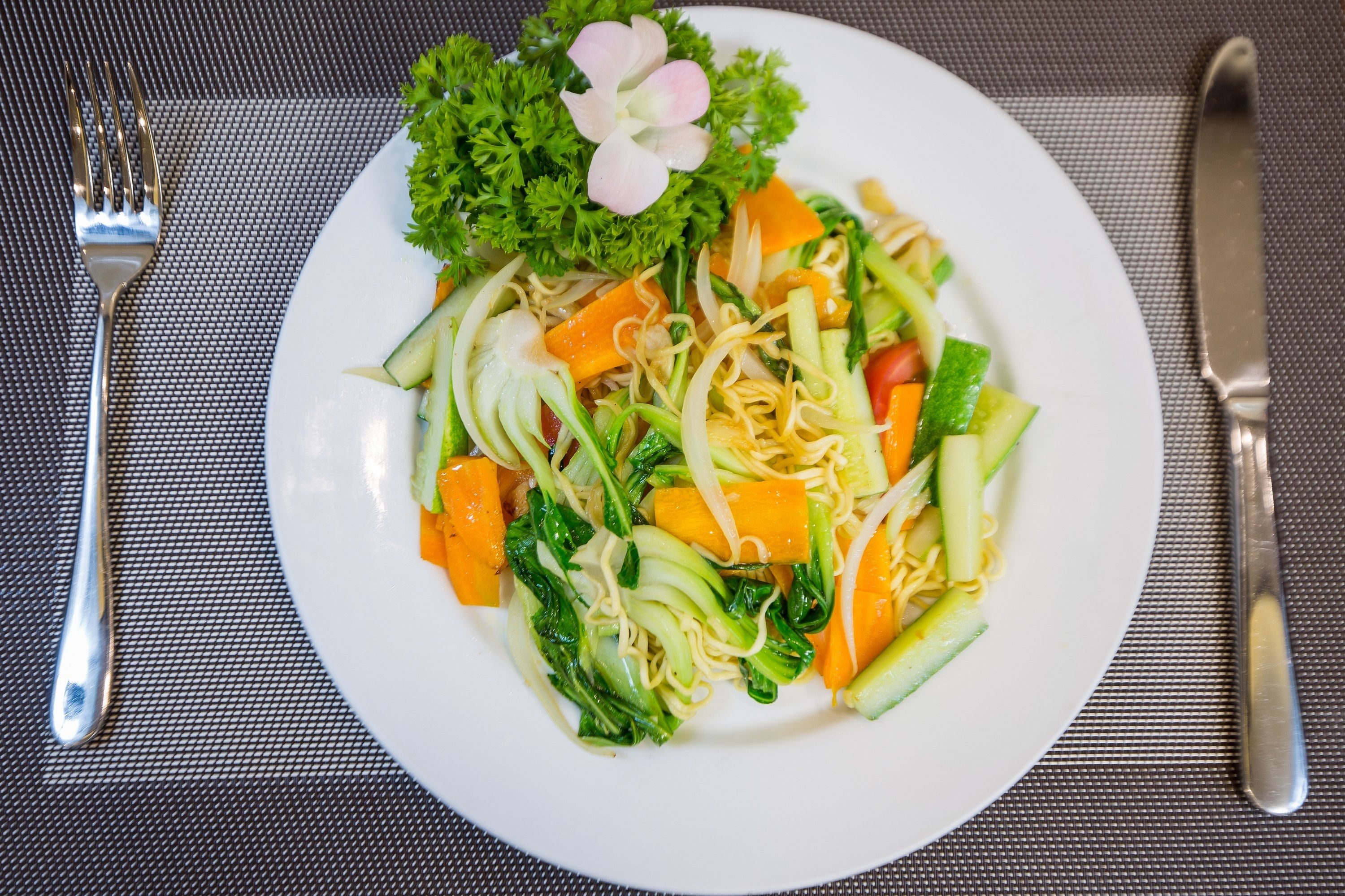 Un plato de fideos con verduras sobre un plato blanco.
