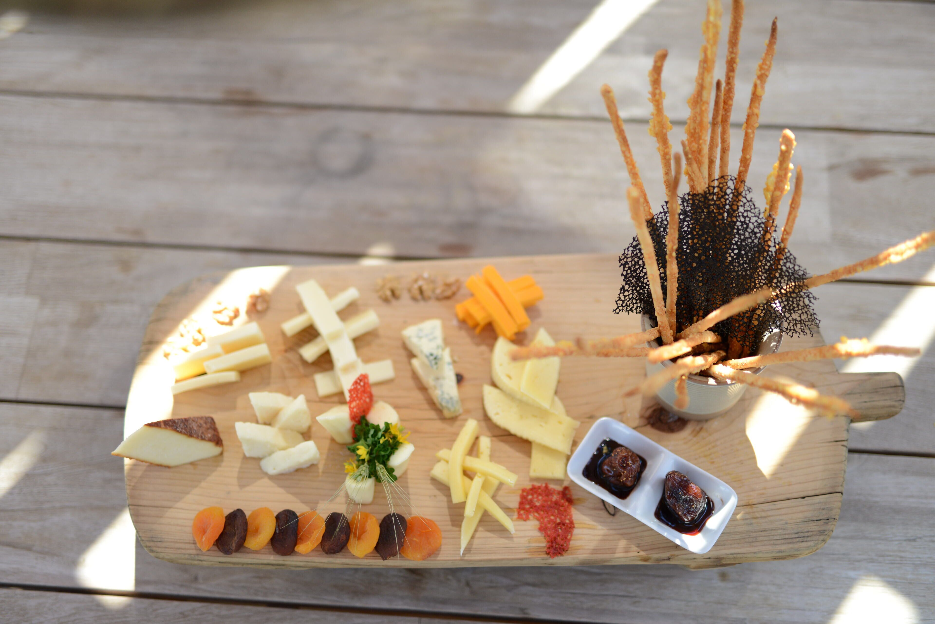 A wooden board with various cheeses, fruits, and crackers.