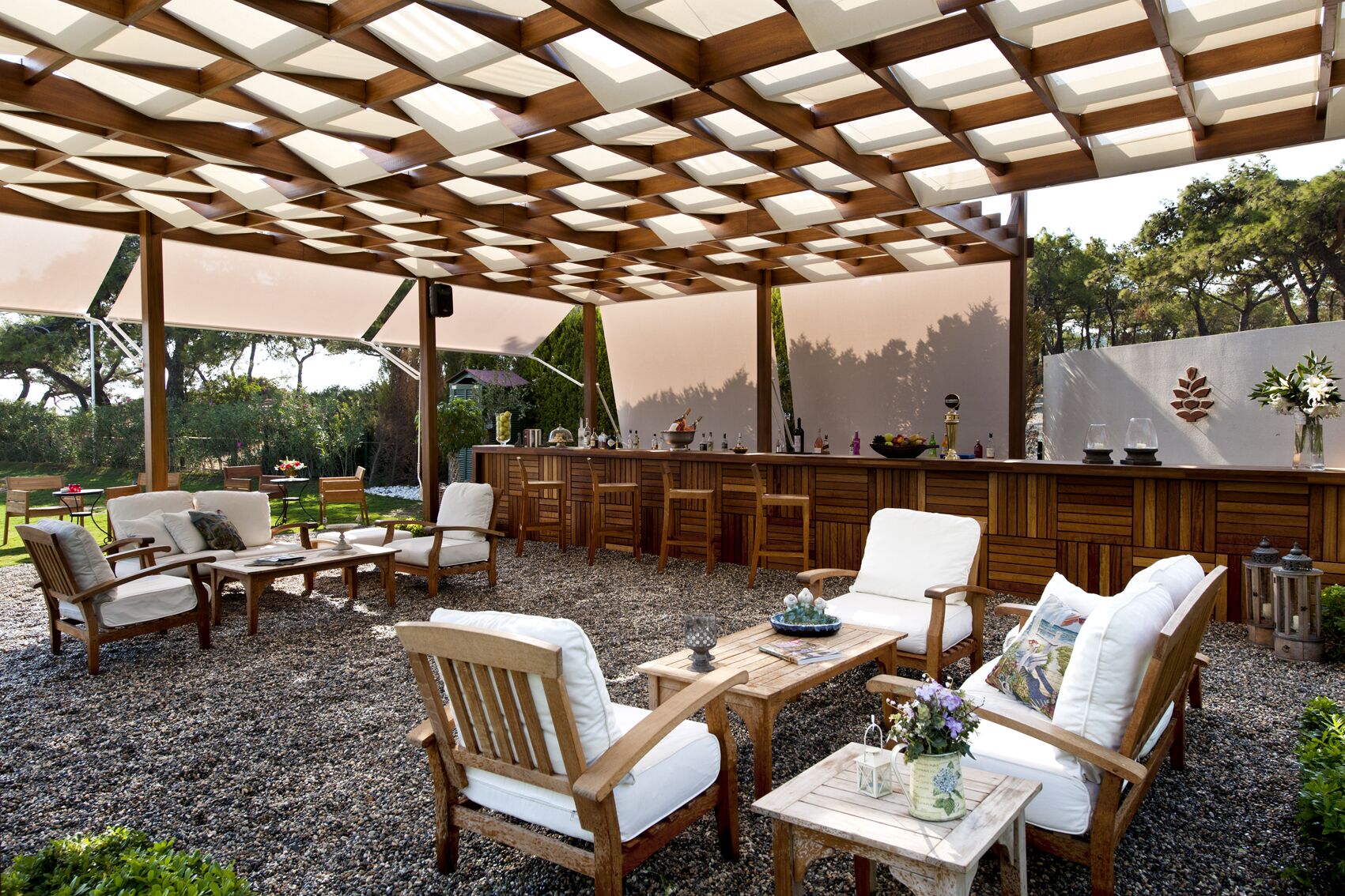An outdoor patio with wooden furniture, a bar area, and a pergola overhead.