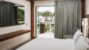 Habitación de hotel con una cama grande, zona de estar con una silla, vistas al exterior y un amplio ventanal con cortinas.