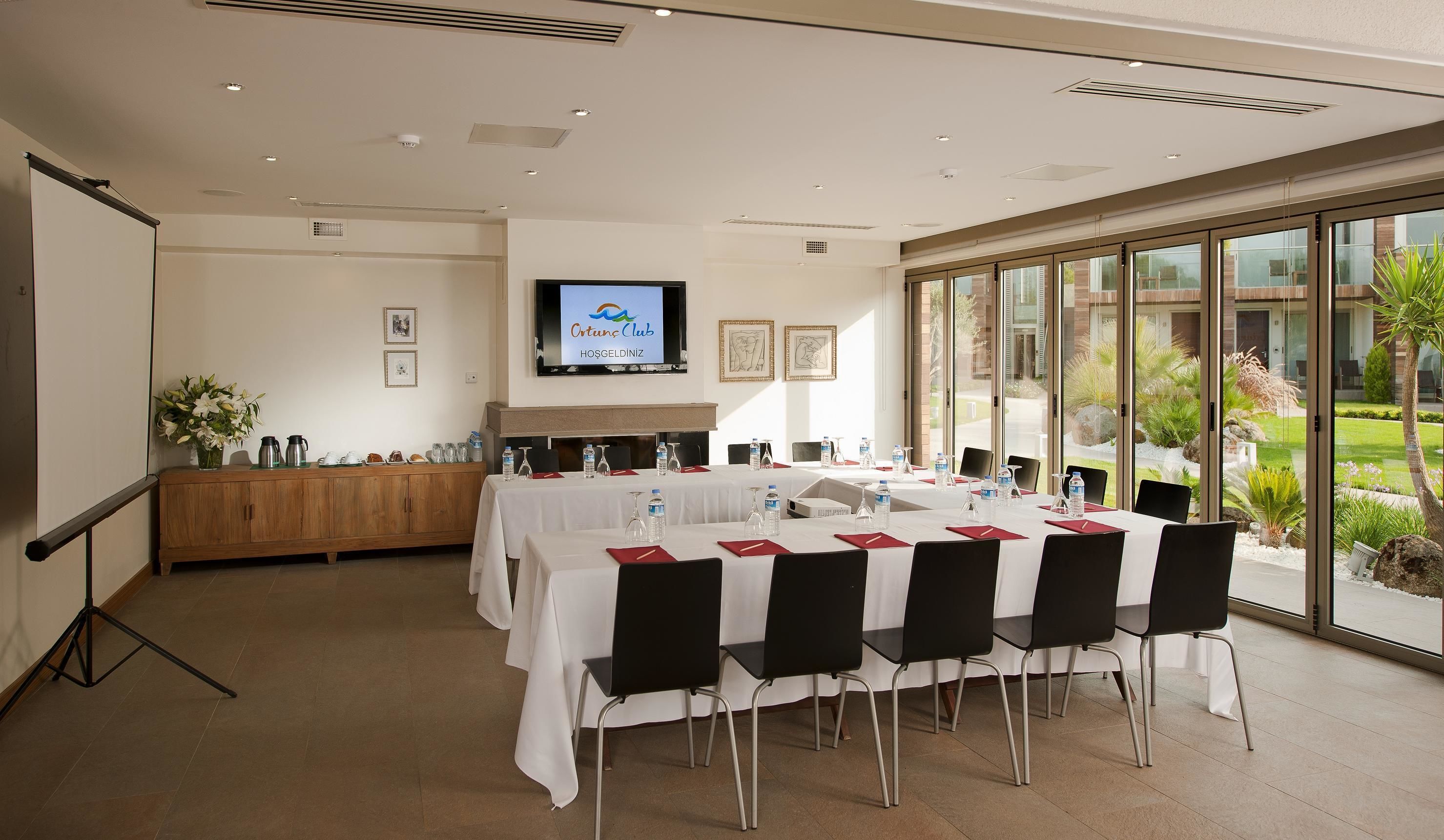 A conference room with a large table, chairs, a TV screen, and a view of a landscaped garden.