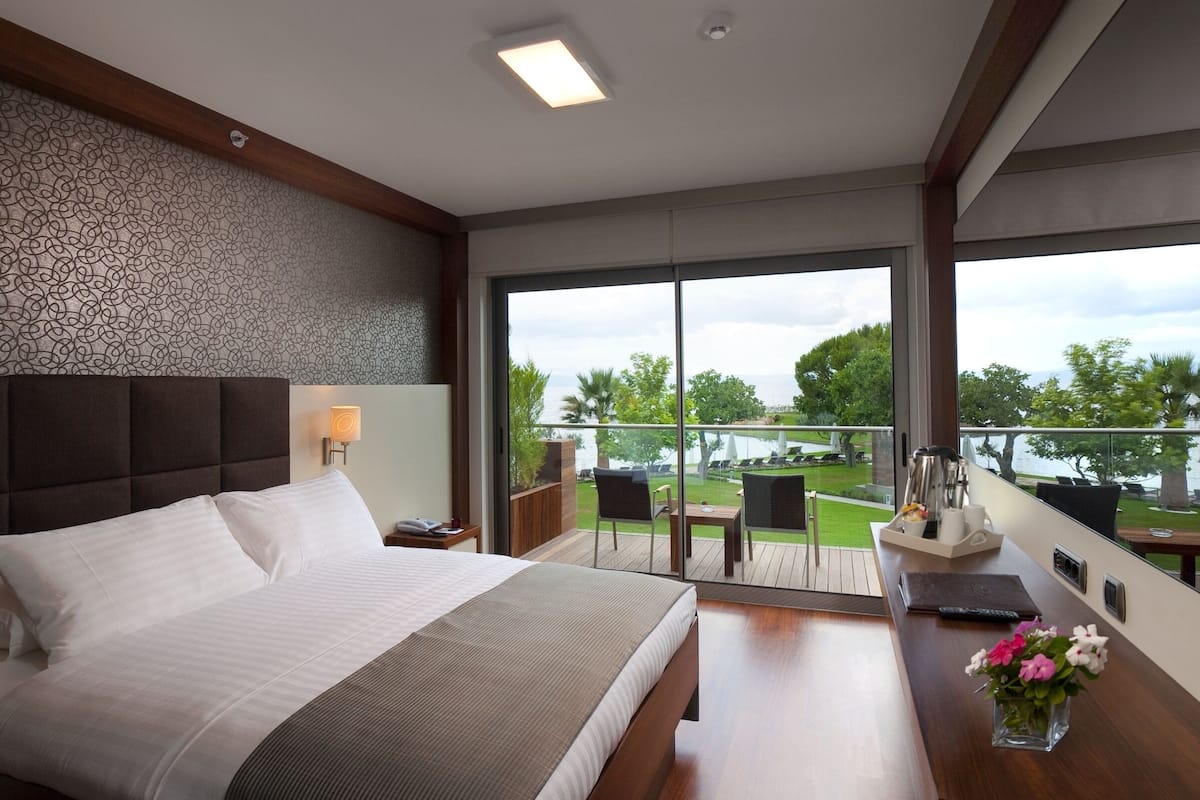 Una habitación de hotel moderna con una cama grande, un escritorio con un florero, un balcón con vistas al mar y una pared con estampado.