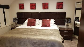 A bedroom with a large bed, two bedside tables with lamps, a headboard, and four red rose paintings on the wall.