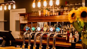 A bar with multiple taps, a cash register, and a variety of bottles in the background. - The Cricketers Arms (Saffron Walden)