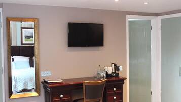 A hotel room with a bed, a desk with a chair, a television, and a door.