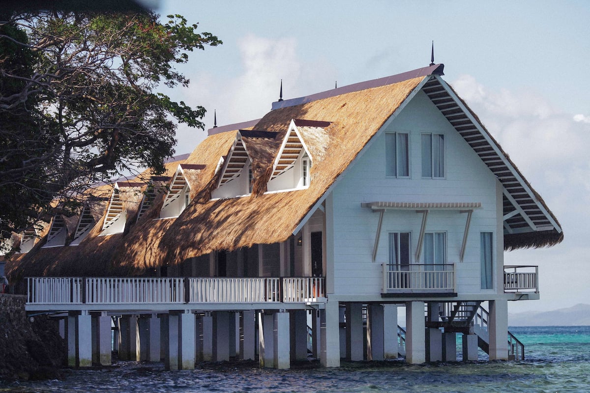 A beachfront house with a thatched roof, a balcony, and a view of the sea.