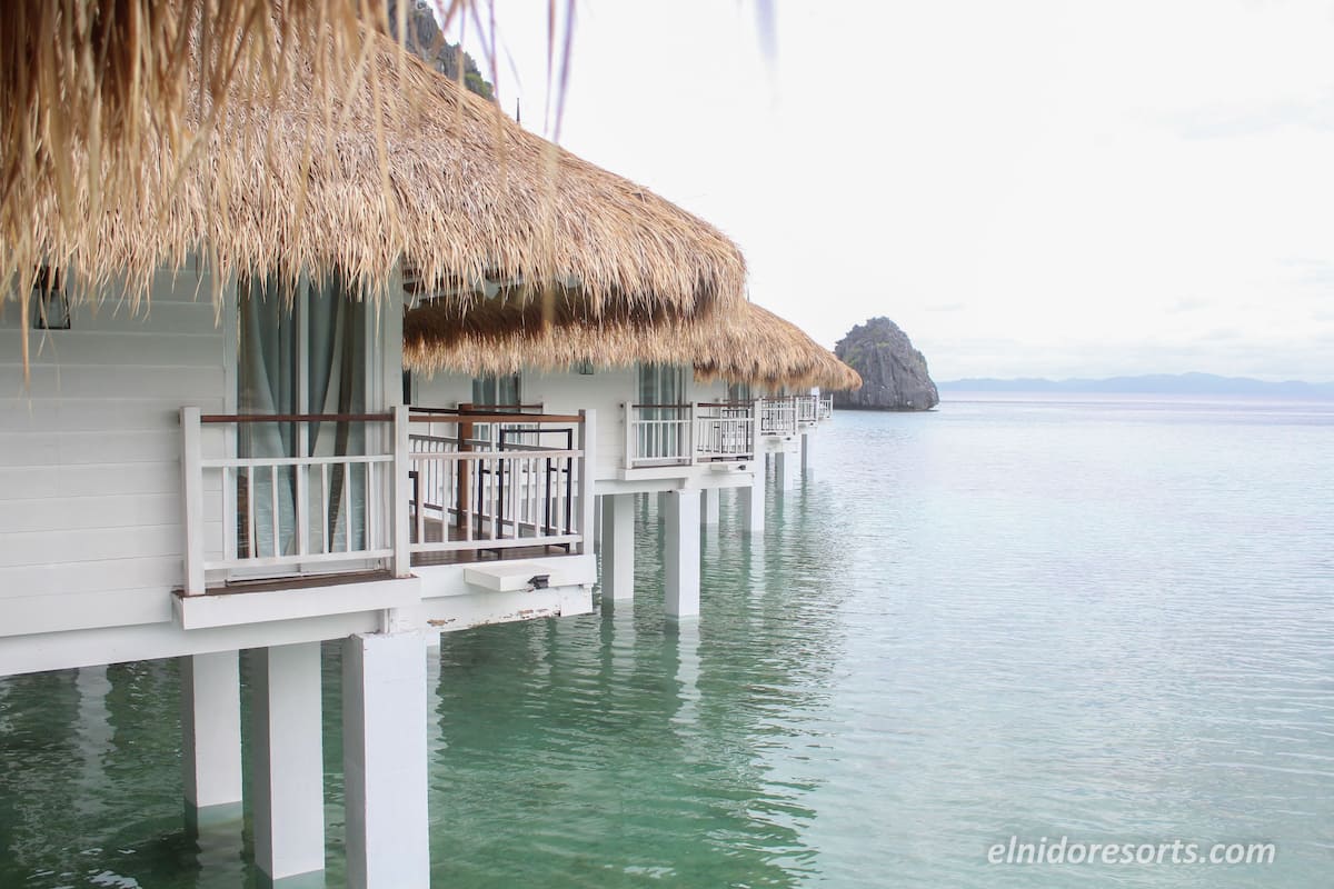 Overwater bungalows with thatched roofs and white railings, connected by walkways over calm water.