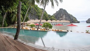 Piscina de resort con palmeras, sillas de playa y sombrillas.