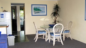 A dining area with a glass table and wicker chairs, a potted plant, and a painting on the wall. - Noosa Keys Resort (Noosaville)