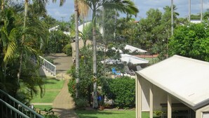 A lush, green outdoor area with palm trees, a pathway, and a building with a white roof. - Noosa Keys Resort (Noosaville)