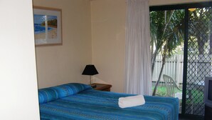 A hotel room with a bed, a nightstand, a lamp, a TV, and a view of the outdoors. - Noosa Keys Resort (Noosaville)