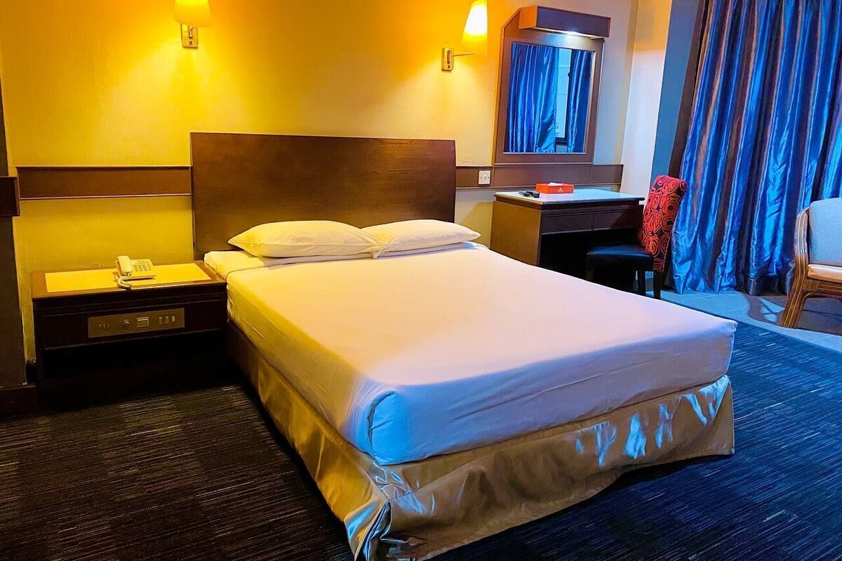 A hotel room with a large bed, bedside tables, a desk, and a chair.