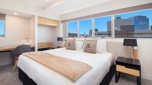 A modern hotel room with a large bed, a desk, and a view of the cityscape.