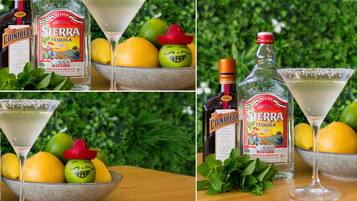 A table with a bottle of Sierra tequila, a glass of tequila, lemons, and a bowl of fruit with a sombrero.