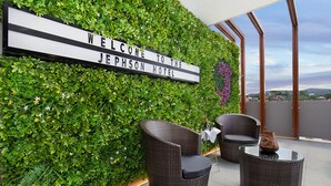 A reception area with a welcome sign, green foliage wall, wicker furniture, and a glass table.