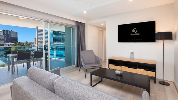 A modern hotel room with a balcony, a flat-screen TV, a sofa, a coffee table, and a TV stand.