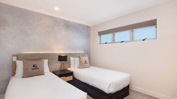 A hotel room with two beds, a window, and a nightstand with a lamp.