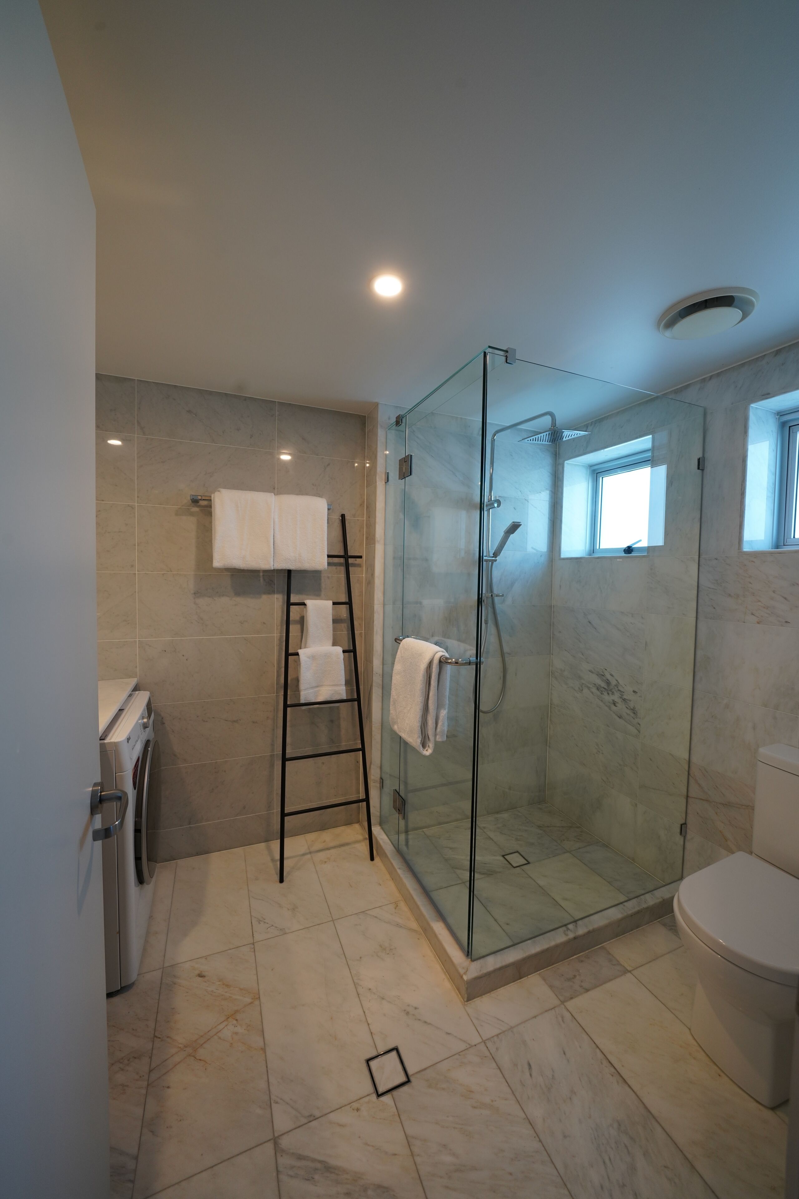 Un baño moderno con ducha envuelta en vidrio, inodoro blanco y lavadora.