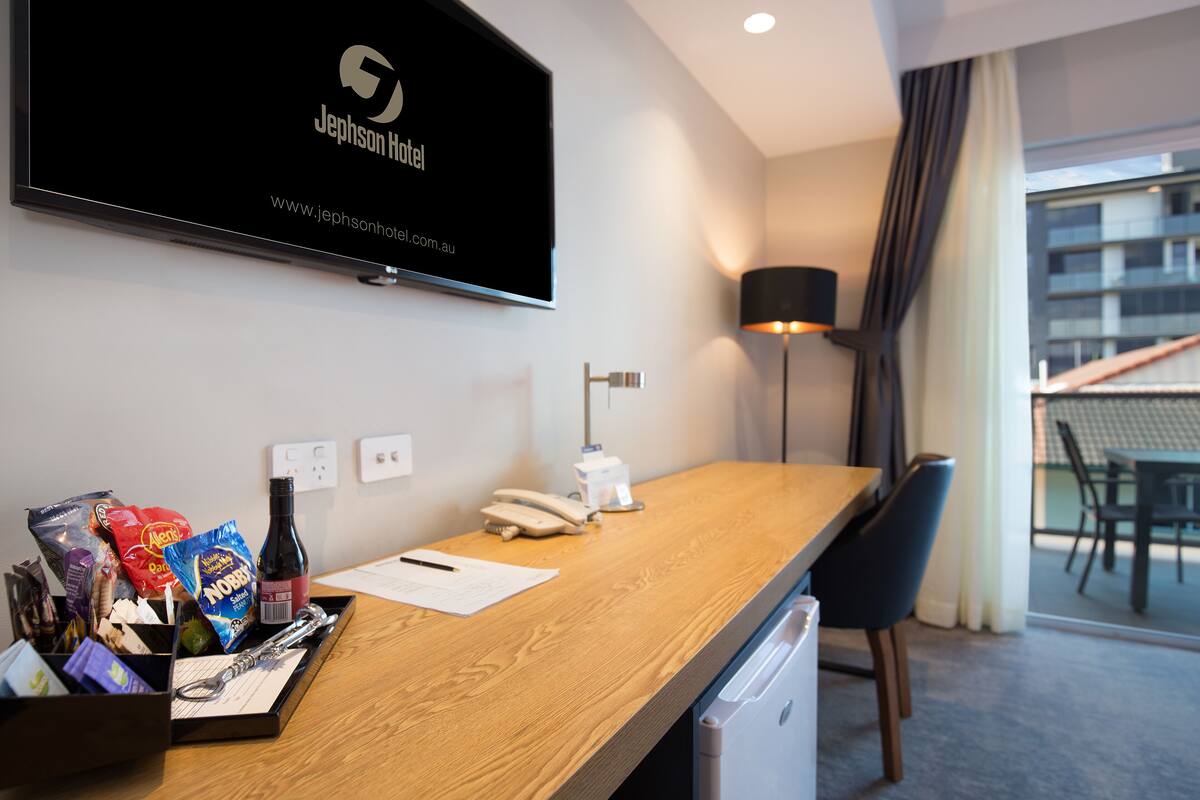 A hotel reception desk with a flat-screen TV displaying the Jephson Hotel logo, a telephone, a notepad, and various snacks.